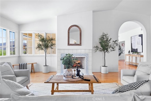 living room with vaulted ceiling, wood finished floors, arched walkways, and a tile fireplace