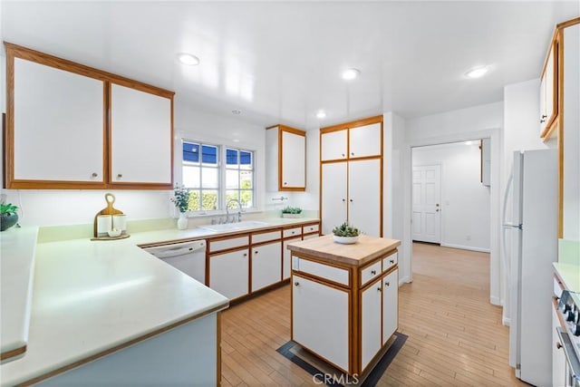 kitchen with white appliances, white cabinetry, light wood-style floors, and a sink