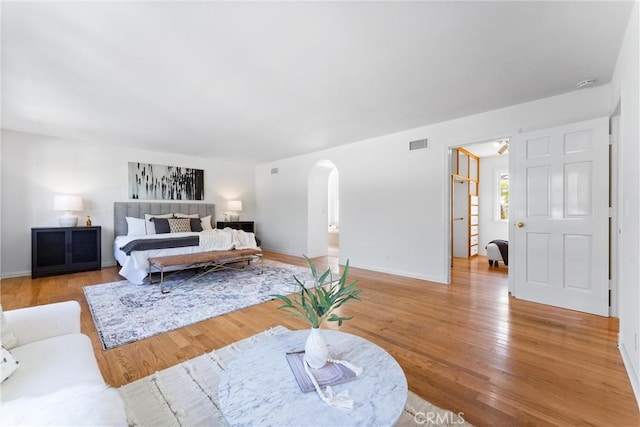 bedroom with baseboards, arched walkways, visible vents, and light wood-type flooring