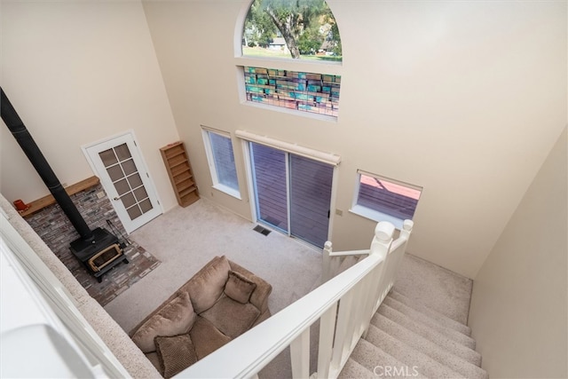 staircase featuring a wood stove, a high ceiling, and carpet flooring