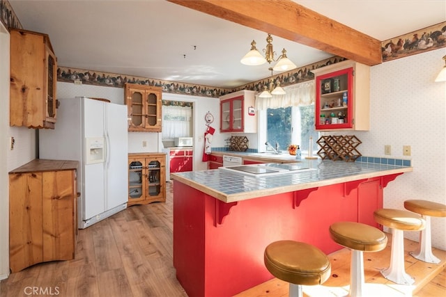 kitchen featuring a breakfast bar, light hardwood / wood-style floors, kitchen peninsula, white appliances, and decorative light fixtures