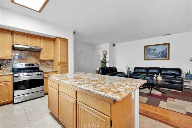 kitchen with light stone countertops, stainless steel gas range oven, a center island, and tasteful backsplash