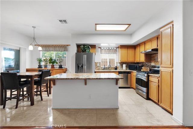 kitchen with decorative light fixtures, appliances with stainless steel finishes, a wealth of natural light, and a center island