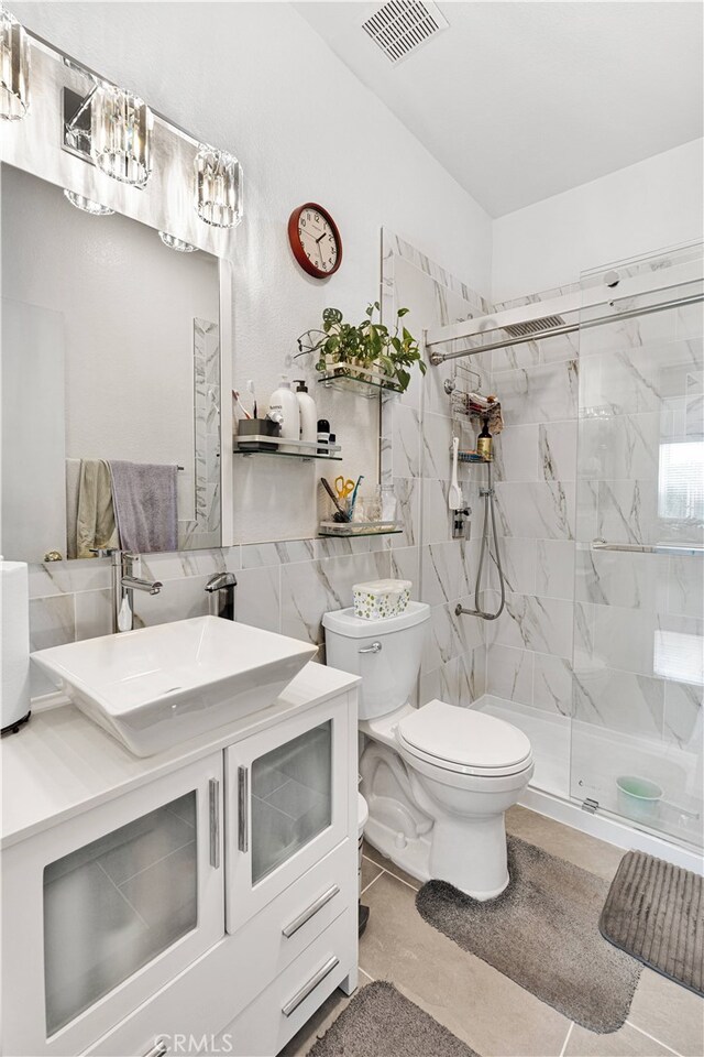 bathroom with tile walls, a shower with door, tile patterned floors, vanity, and toilet