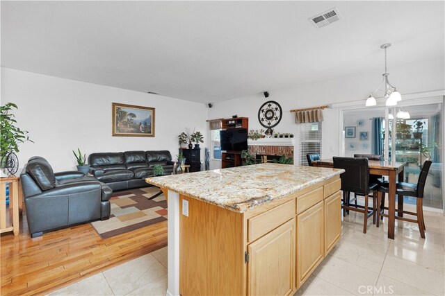 kitchen with light hardwood / wood-style floors, a brick fireplace, an inviting chandelier, a center island, and decorative light fixtures