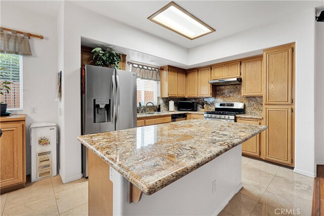 kitchen with sink, tasteful backsplash, stainless steel appliances, a center island, and light stone countertops