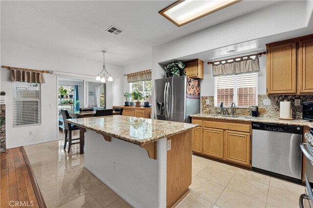 kitchen with a wealth of natural light, a center island, appliances with stainless steel finishes, and decorative light fixtures