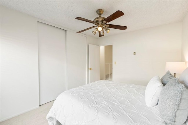 bedroom with ceiling fan, a textured ceiling, light carpet, and a closet