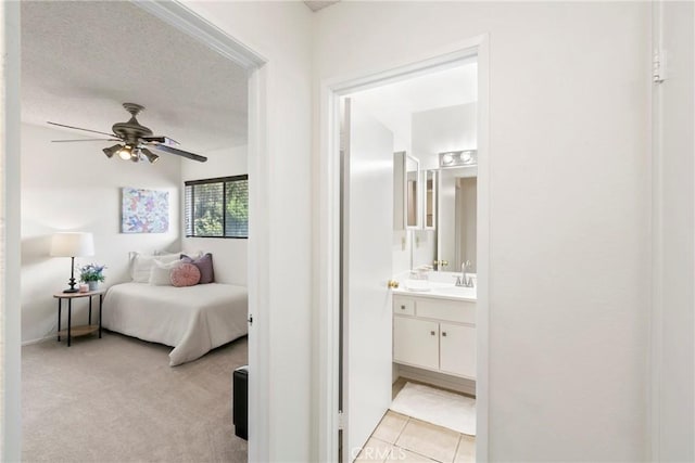 bedroom featuring a textured ceiling, connected bathroom, light colored carpet, and ceiling fan