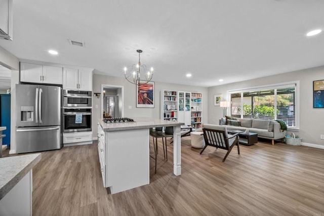 kitchen with white cabinetry, hanging light fixtures, stainless steel appliances, a breakfast bar area, and light wood-type flooring