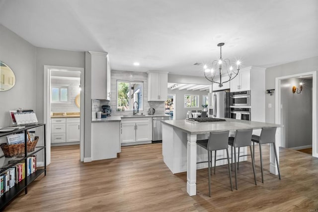 kitchen featuring white cabinets, stainless steel appliances, a kitchen island, and light hardwood / wood-style flooring