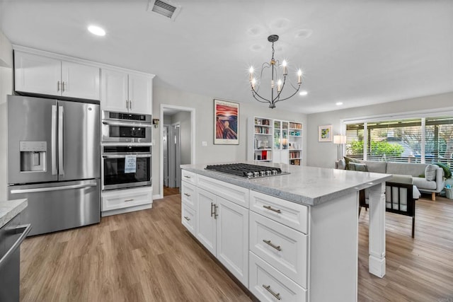 kitchen featuring white cabinets, appliances with stainless steel finishes, light hardwood / wood-style floors, and decorative light fixtures