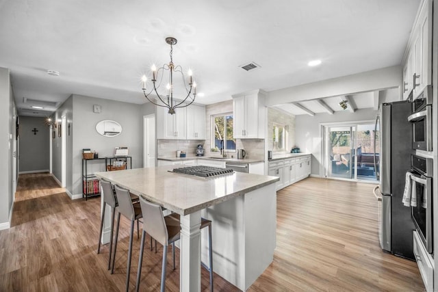 kitchen featuring beam ceiling, white cabinets, decorative light fixtures, and light wood-type flooring