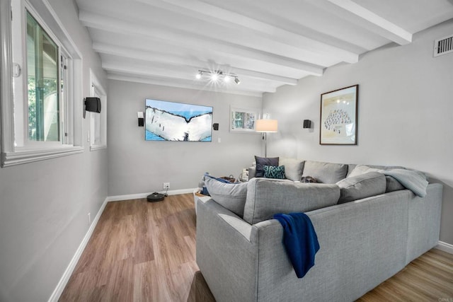 living room with beam ceiling, light wood-type flooring, and plenty of natural light