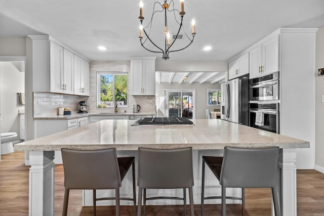 kitchen featuring stainless steel appliances, beam ceiling, decorative light fixtures, white cabinets, and a center island