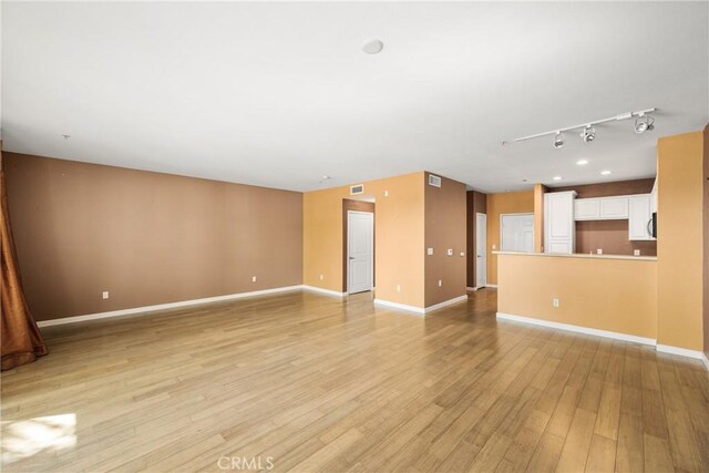 unfurnished living room featuring rail lighting and light hardwood / wood-style floors