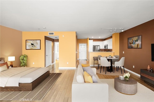 bedroom with visible vents, light wood finished floors, freestanding refrigerator, and baseboards