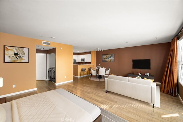 living area with light wood finished floors, washing machine and dryer, visible vents, and baseboards