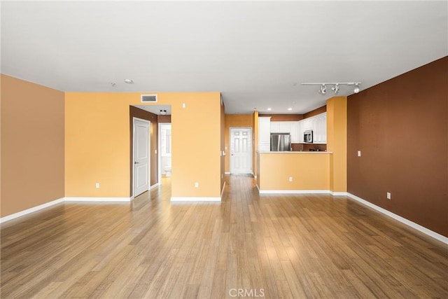 unfurnished living room with light wood-type flooring, rail lighting, baseboards, and visible vents