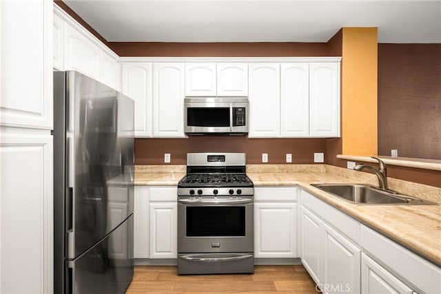 kitchen with white cabinets, light wood finished floors, stainless steel appliances, and a sink