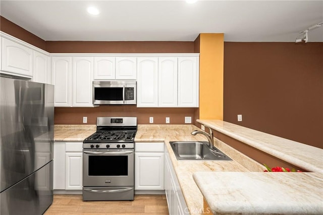 kitchen featuring a peninsula, a sink, white cabinets, light countertops, and appliances with stainless steel finishes