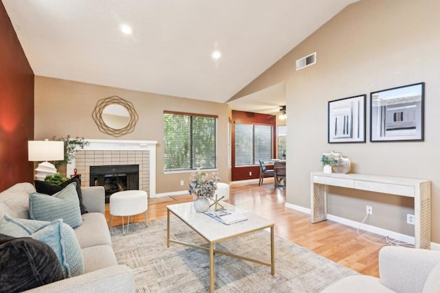 living room with light hardwood / wood-style floors, ceiling fan, lofted ceiling, and a tiled fireplace