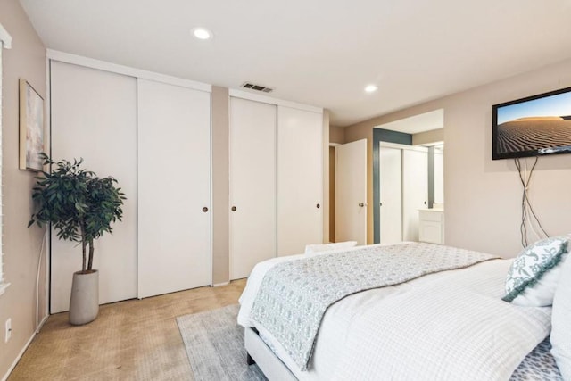 bedroom featuring two closets, light colored carpet, and ensuite bath