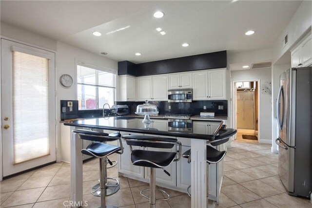 kitchen featuring a kitchen bar, appliances with stainless steel finishes, tasteful backsplash, light tile patterned floors, and white cabinets