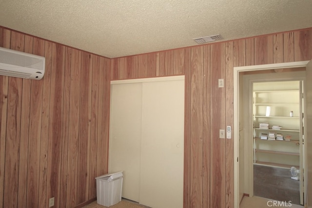 unfurnished bedroom featuring wooden walls, a closet, a textured ceiling, and an AC wall unit