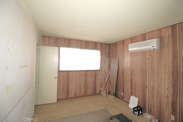 spare room featuring light colored carpet, a textured ceiling, wooden walls, and an AC wall unit