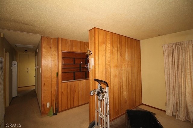 hallway featuring wooden walls, a textured ceiling, and light colored carpet