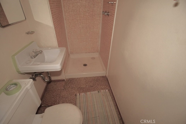 bathroom featuring a tile shower, sink, and toilet