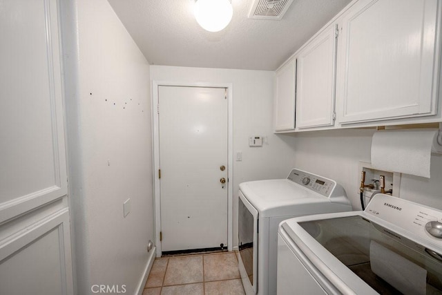 clothes washing area with washing machine and dryer, light tile patterned floors, cabinets, and a textured ceiling