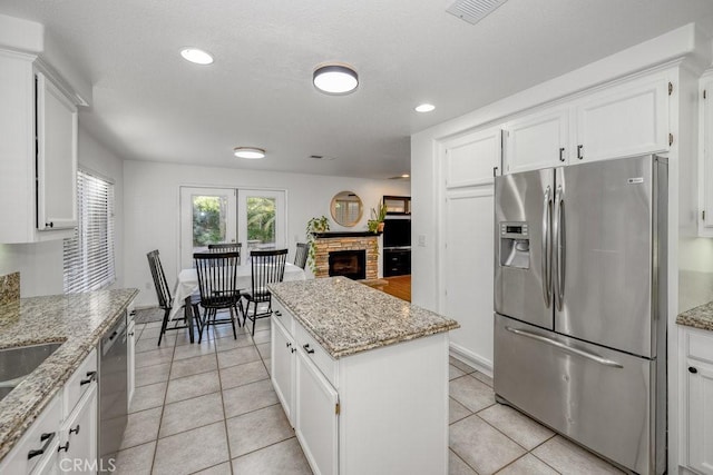 kitchen featuring white cabinets, stainless steel appliances, a stone fireplace, visible vents, and light tile patterned flooring