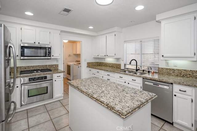 kitchen with sink, stainless steel appliances, a kitchen island, light stone counters, and white cabinets