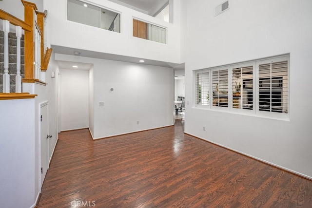 unfurnished living room with a towering ceiling and dark wood-type flooring