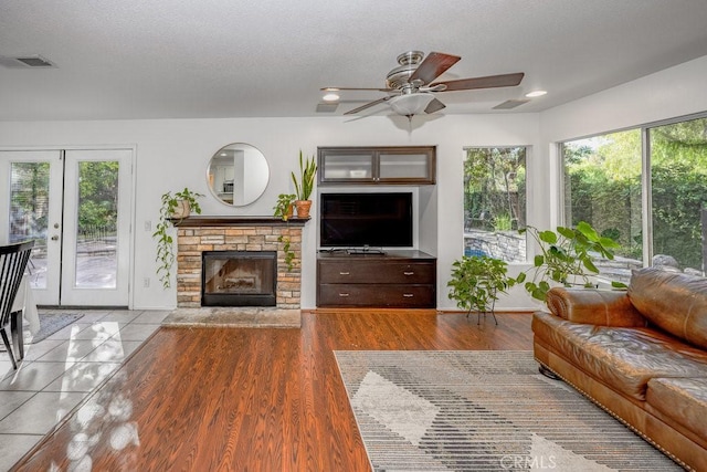 living room with french doors, ceiling fan, light wood-type flooring, a textured ceiling, and a fireplace