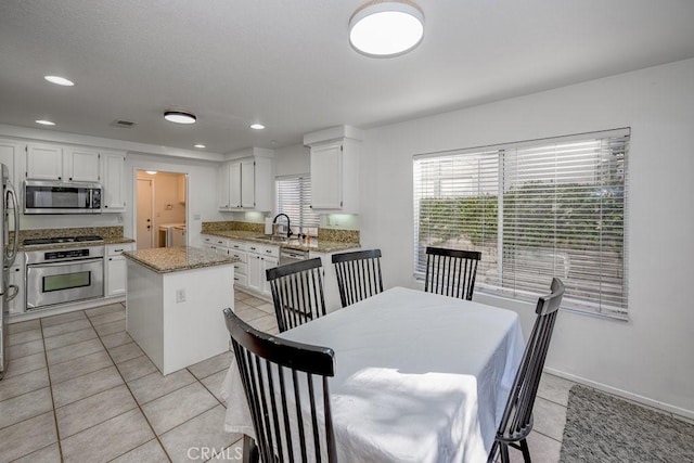 kitchen with stainless steel appliances, washer and clothes dryer, sink, a center island, and white cabinetry