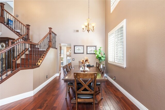 dining space with a towering ceiling, an inviting chandelier, and dark wood-type flooring