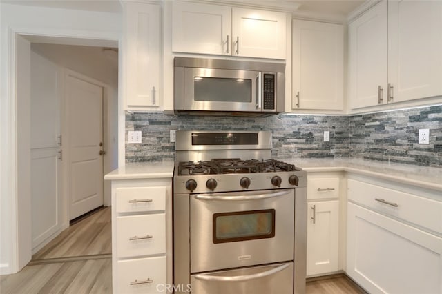 kitchen with stainless steel appliances, white cabinetry, light wood-type flooring, and tasteful backsplash