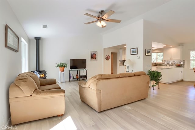 living room featuring ceiling fan, light hardwood / wood-style flooring, a wood stove, and sink