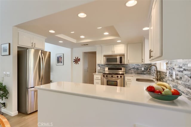 kitchen with white cabinetry, kitchen peninsula, stainless steel appliances, light wood-type flooring, and sink