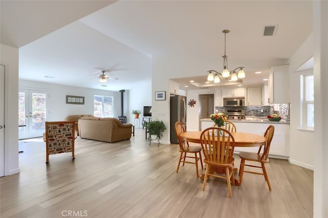 dining area featuring ceiling fan with notable chandelier, a wood stove, light hardwood / wood-style floors, and french doors