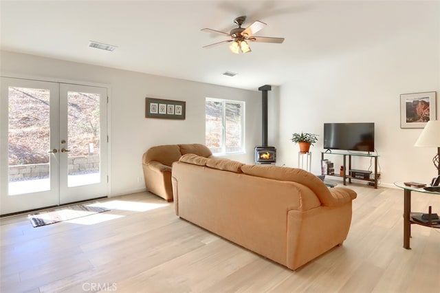 living room featuring french doors, light wood-type flooring, a wood stove, and ceiling fan