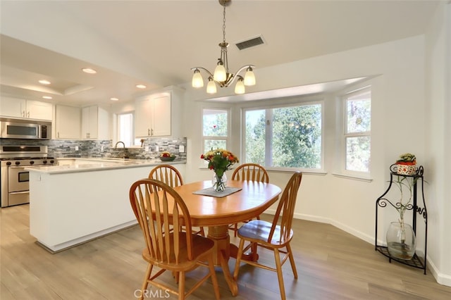 dining area with a notable chandelier, light wood-type flooring, and a tray ceiling