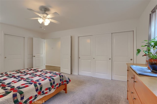 bedroom with two closets, light carpet, and ceiling fan