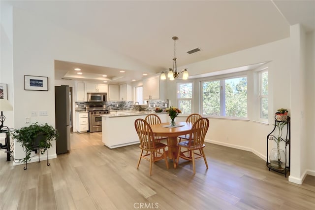 dining space featuring lofted ceiling, an inviting chandelier, light hardwood / wood-style flooring, and sink