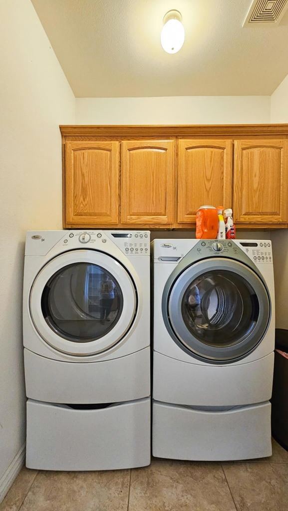 clothes washing area with light tile patterned floors, cabinets, and independent washer and dryer