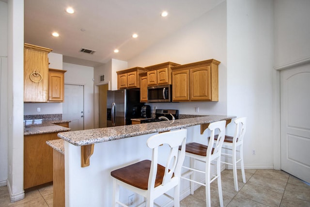 kitchen with kitchen peninsula, appliances with stainless steel finishes, a breakfast bar area, light stone countertops, and vaulted ceiling