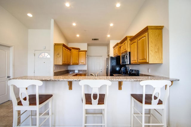 kitchen featuring light stone countertops, stainless steel appliances, kitchen peninsula, and a breakfast bar area